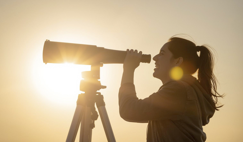 Fotografía de una muchacha mirando un telescopio.