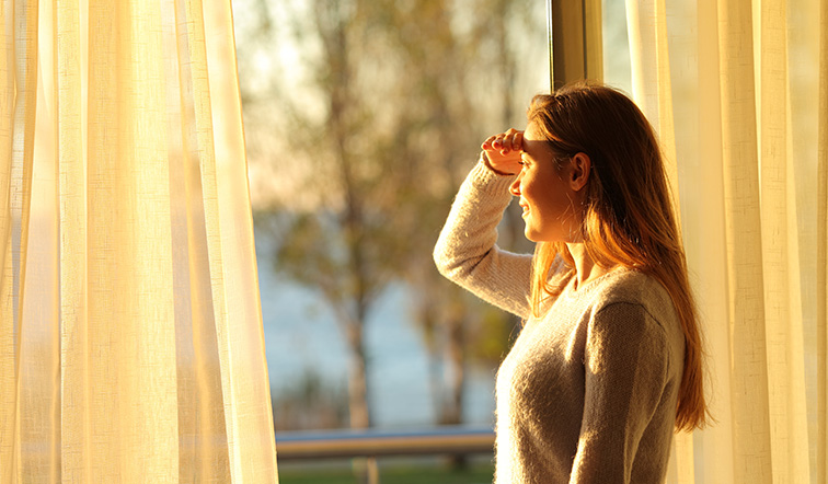 Happy teen scouting through a window at home.