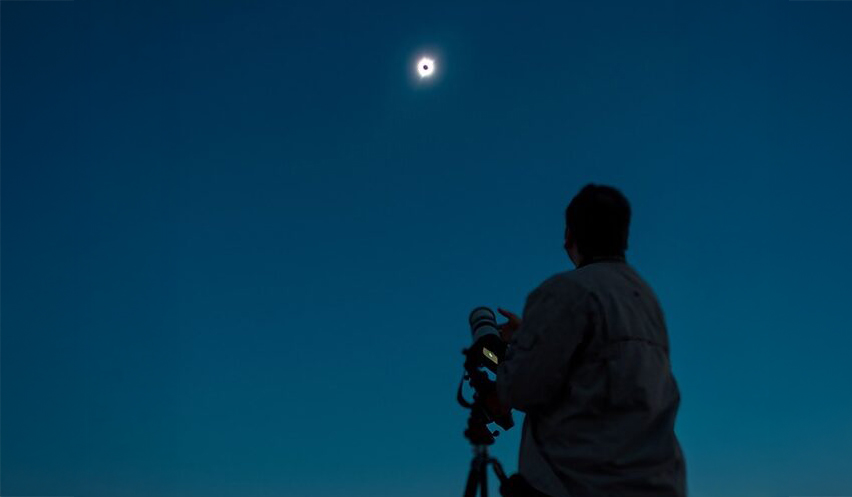 Imagen de un cielo azul con una persona observando a través de un telescopio.
